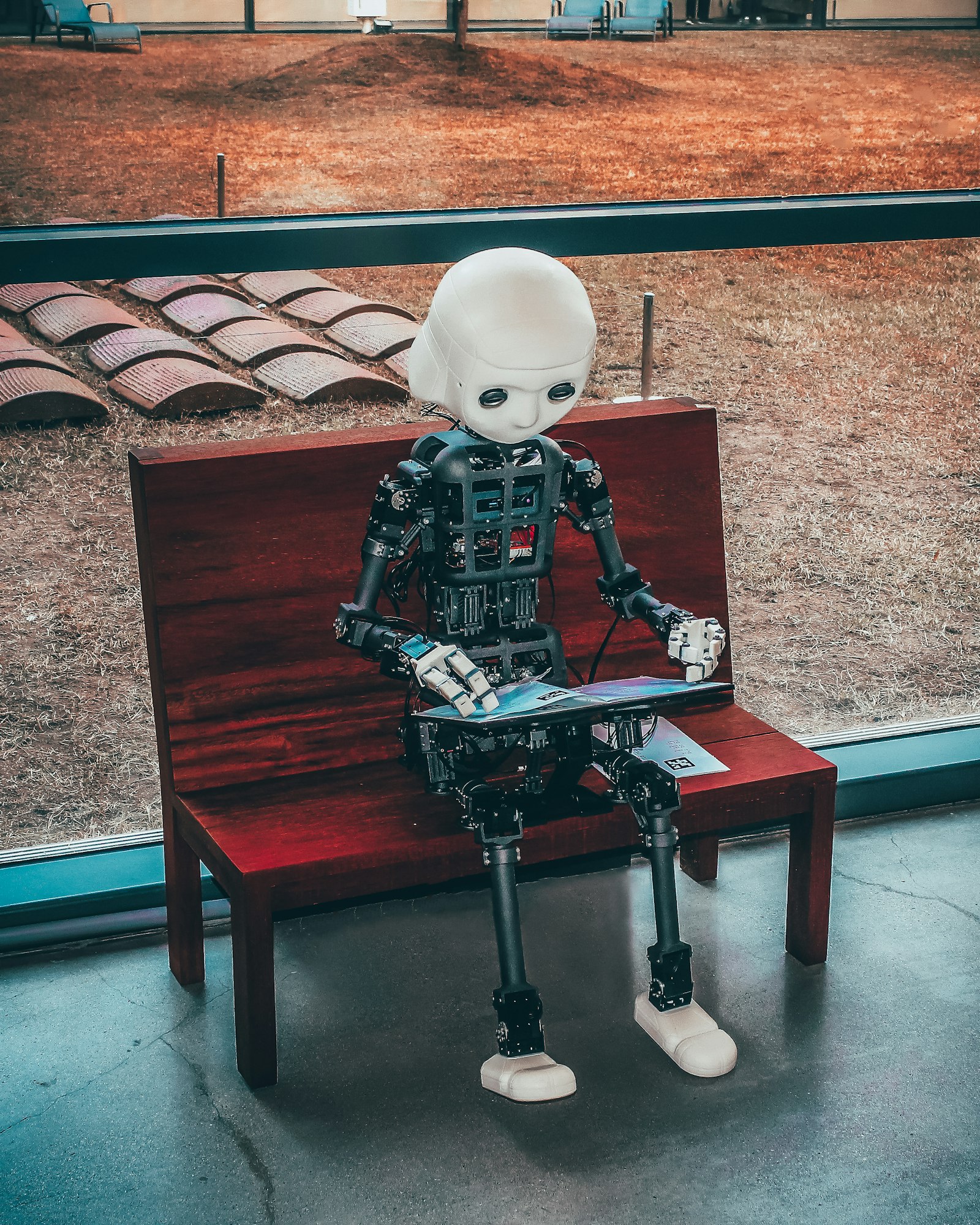 Small humanoid robot sitting on a bench reading